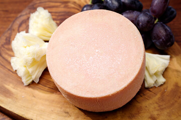 Traditional tete de moine aged mountain cheese of the Alps offered with grapes on a wooden board