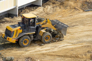 Fototapeta na wymiar Bulldozer unloads stones at a construction site. A yellow tractor with a bucket conducts construction work. Road construction.