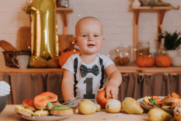 smiling one-year-old baby boy in festive clothes holds an apple in his hands. first birthday. body with the number one. golden foil ball. healthy snack for kids. little chef. High quality photo