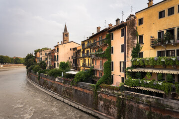 Fototapeta na wymiar Colorful facades of the old town buildings by the Adige river from the stone bridge on a cloudy day, Verona, Veneto Region, Italy