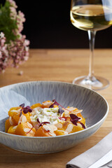 baked pumpkin in ceramic plate on wooden table with glass of white wine. pumpkin with stracciatella and microgreen