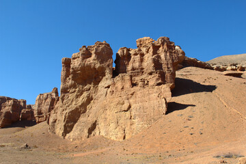 Large relief sandy-clay rock of the red Charyn canyon in Altyn-Emel, mountain slopes, other rocks in the distance, sky with clouds, summer, sunny