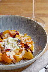 baked pumpkin in ceramic plate close up wooden table with glass of white wine. pumpkin with stracciatella and microgreen