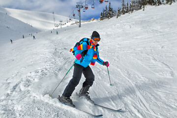 Young guy skier turning in powder snow; blue jacket; black pant