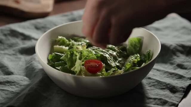Slow motion man add cherry tomatoes to romaine leaves in white bowl