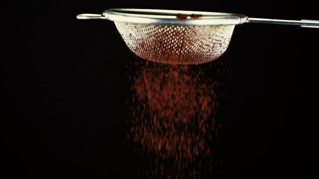 Chocolate and cocoa. Sifting dark cocoa powder through sieve, on a black background, slow motion shot.