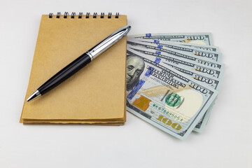 Craft notebook, on the notebook is a premium pen, under the notebook are American 100 dollar bills. Close up, selective focus. 
