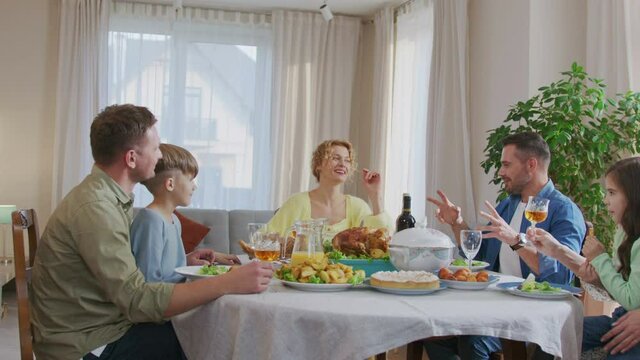 Caucasian people clinking glasses with each other while sitting at dining table, feeling happy and cheery smiling. Party concept