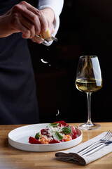 The chef prepares a salad with salmon. Rubs cheese on a grater. salmon salad with beet cheese and green leaves on wooden table with glass of white wine.