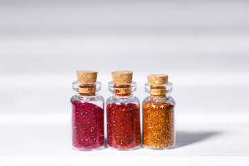 Small Glass jars with pink, orange and red glitters for nail art and makeup on white background, Copyspace