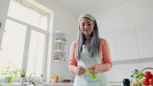 Middle aged lady make husband supper add salad green fresh leaf in kitchen