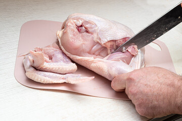 A man carves a fresh chicken with a kitchen knife.