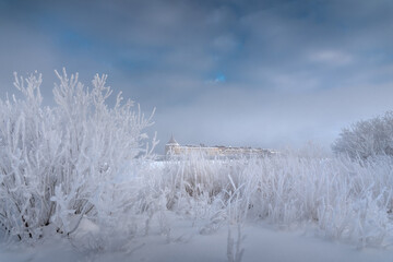 Snow-white crystal winter background. Trees and grass are covered with heavy frost. Beautiful clouds in the blue sky. An old fortress in the background. Ladoga lake. Shlisselburg.