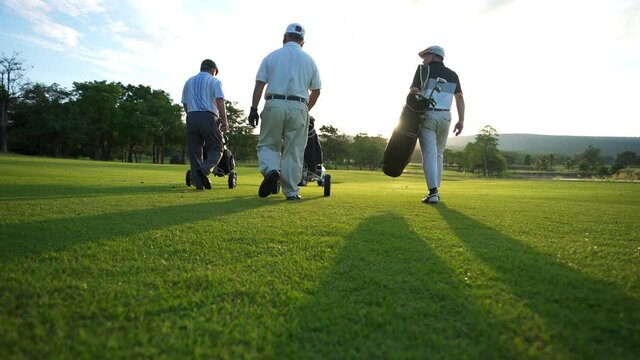 4K Group of Asian people businessman and senior CEO enjoy outdoor sport golfing together at country club. Healthy men golfer holding golf bag walking on fairway with talking together at summer sunset