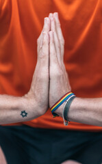 Hands of a man with a rainbow bracelet gesturing gratitude doing yoga