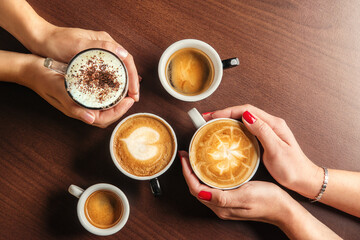 Cups of coffee in the hands of men and women. coffee break on a wooden background. with copy space. top view