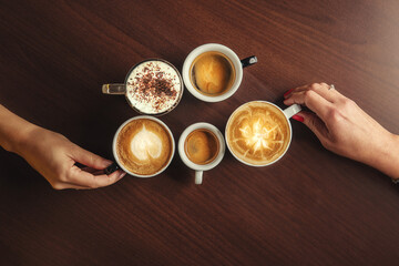 Cups of coffee in the hands of men and women. coffee break on a wooden background. with copy space. top view