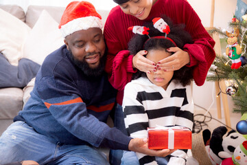 Fototapeta premium Happy family father and mother close eye daughter and giving gift box on celebration in Christmas day at home, xmas with parent surprising children at house, thanksgiving eve, Merry Christmas.