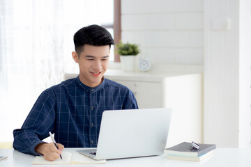 Fototapeta premium Young asian business man writing on notebook for planning working and using laptop computer on desk at home, notes about finance, male study and learning, business and communication concept.