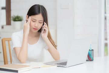 Young asian woman working on laptop computer and talking smartphone having stress and upset at home, girl having problem and worried, frustrated and unhappy, business and communication concept.