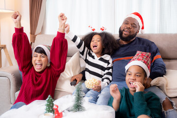 Happiness African family watching movie with excited and fun in the living room for leisure with comfort at home on Christmas day, dad and mom and daughter cheering watching tv with victory.