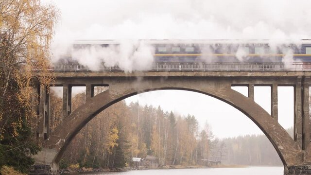 Steam locomotive with smoke from a chimney on a bridge over a river in Karelia