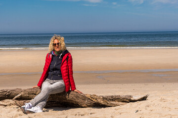Blonde woman sitting in the wind on a tree on the beach