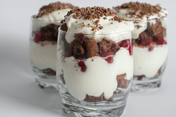 Biscuit cake with cream and cherries in a glass on a white background