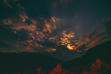 The orange moon rising from behind the mountain range illuminates the misty clouds, creating a mystical atmosphere.supermoon.the rising moon in the gorge of the Caucasus Mountains.defocusing,in motion