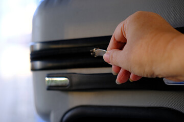 close-up of female hand zips the metal zipper of a silvery modern suitcase, concept of summer...