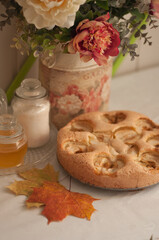 a round homemade apple pie lies on the table next to yellow autumn leaves in an upright position