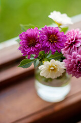 dahlia flowers stand in a jar with water on the window in a vertical format