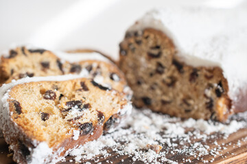 Traditional Christmas stollen made of dried fruits and nuts sprinkled with powdered sugar on the background of a Christmas decor with candles. Traditional Christmas cupcake