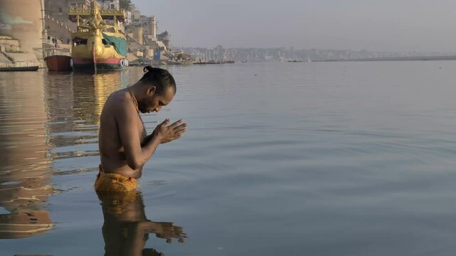 A Hindu priest or pandit standing in the water on the banks of the Ganges, bowing before the Sun in the morning and offering Suryanamaskar, and praying to the morning sun on the banks of  Varanasi.