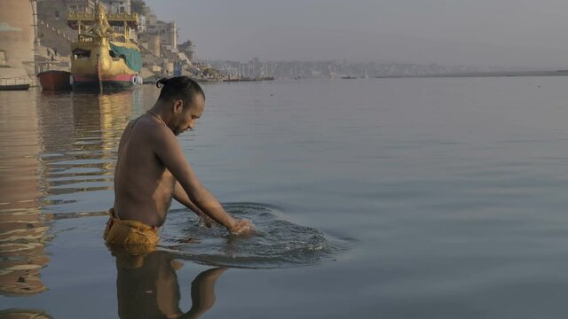 A Hindu priest or pandit standing in the water on the banks of the Ganges, bowing before the Sun in the morning and offering Suryanamaskar, and praying to the morning sun on the banks of  Varanasi.