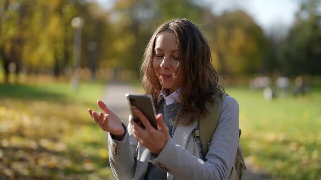 Portrait of an attractive European woman dressed in casual clothes and using a smartphone in a city park. Communicating with people online, exchanging messages and browsing the Internet.