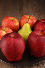 Red apples fruits on black plate. Yellow pear.