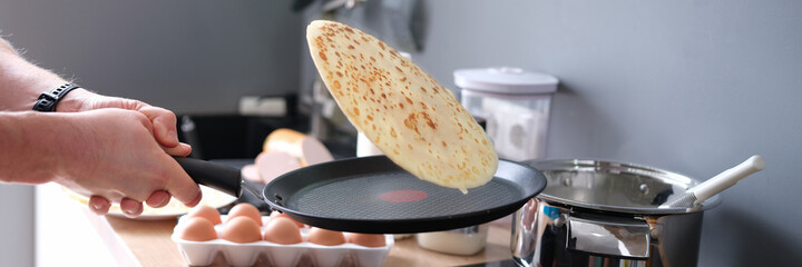 Male chef tossing pancake in frying pan in kitchen closeup - obrazy, fototapety, plakaty