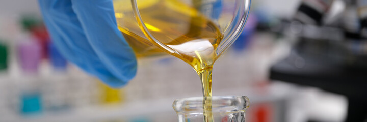 Chemist pouring edible oil from flask into test tube closeup
