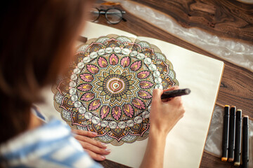 Young beautiful girl with long hair draws a circular mandala pattern.