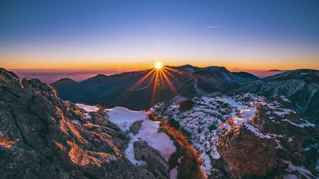 Beautiful sunbeam light of sun at sunrise in alps mountains landscape in autumn morning nature with first snow on rocky peak Time lapse