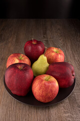Red apples and yellow pear fruits on black plate.