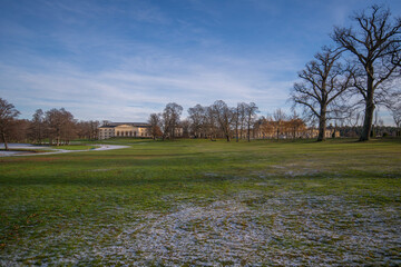 Park view at the Drottningholm island with palace and opera house, frozen meadow and trees a Pale...