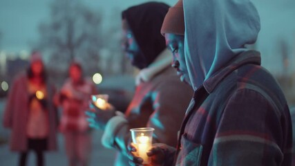 Selective focus shot of two African American men standing outdoors and holding candles in cups while gathering for candlelight vigil