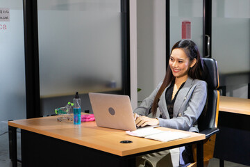 Obraz na płótnie Canvas Young asian businesswoman executive using smartphone with laptop sitting at work desk in office building.