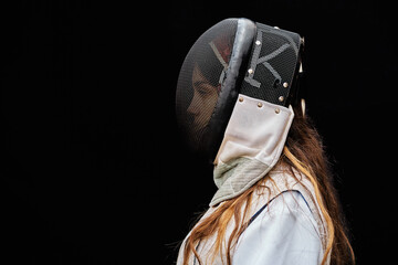 Portrait of woman dressed in white fencing costume practicing with the sword on black background.