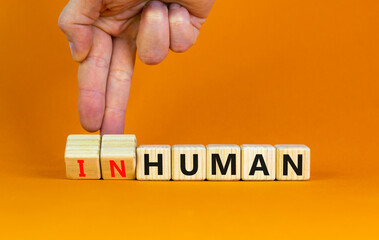 Human or inhuman symbol. Businessman turns wooden cubes and changes the word inhuman to human. Beautiful orange table orange background, copy space. Business, human or inhuman concept.