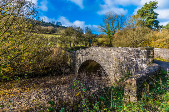 A view of a stone bridge over the Manifold river in the Manifiold valley next to the village of Wetton, UK on a sunny Autumn day