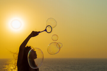 Caucasian girl blowing soap bubbles by the sea at sunset.