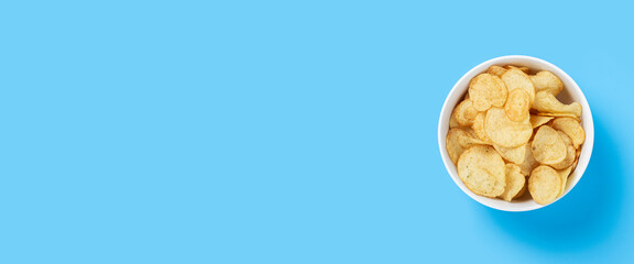 Potato chips in a bowl on a blue background. Top view, flat lay. Banner.